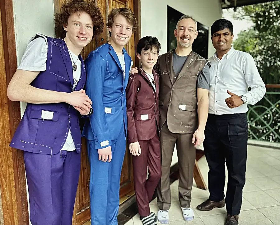 A father and three sons at the basted fitting: four suits half-made in white basting thread, chalk marks and fitting tags still pinned on.