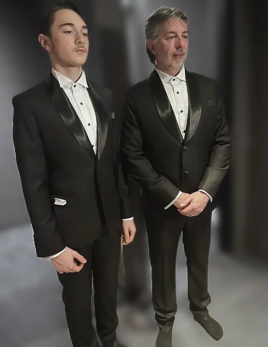 Father and son in black tie — shawl-collar dinner jackets, pleated dress shirts and studs, one waistcoated — in their hotel room.