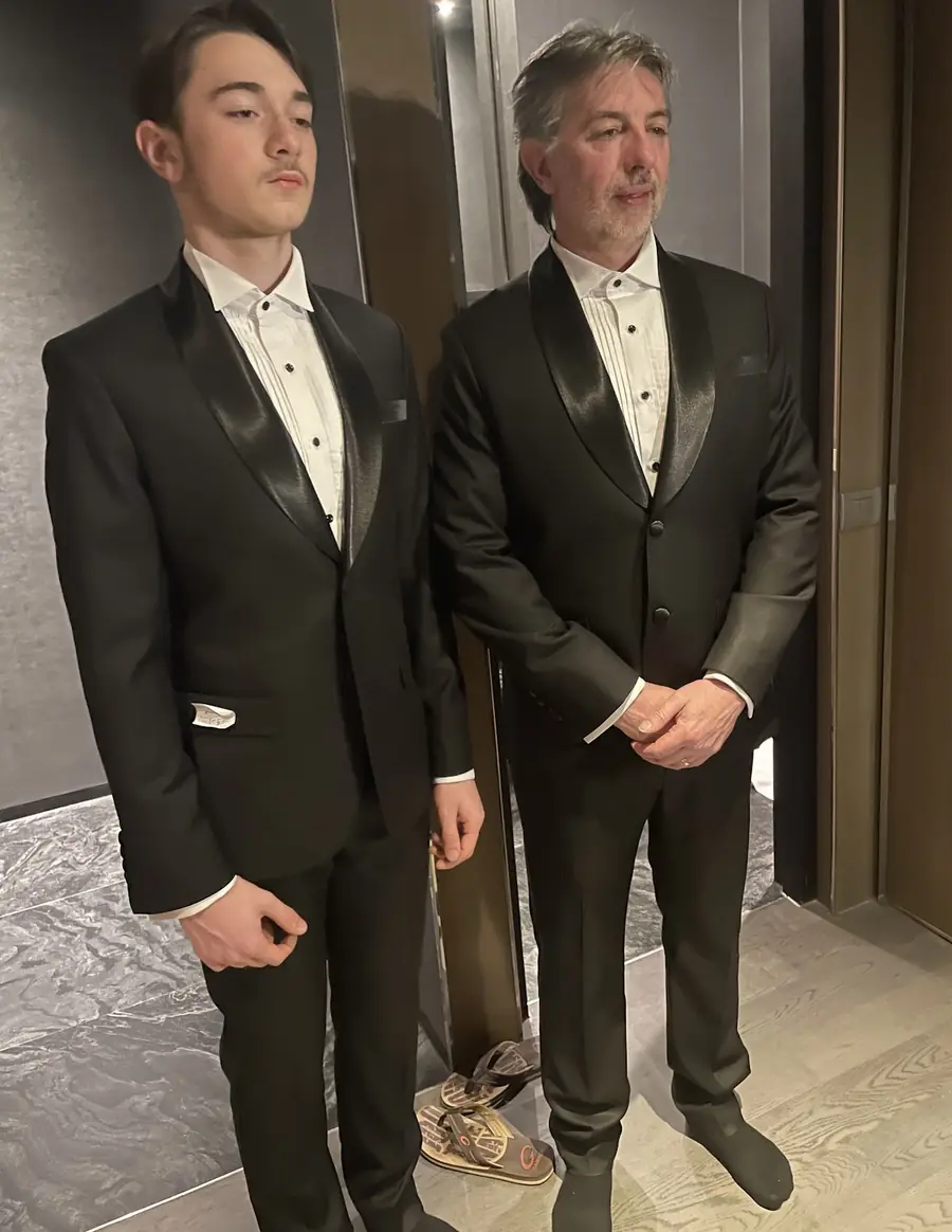 Father and son in black tie — shawl-collar dinner jackets, pleated dress shirts and studs, one waistcoated — in their hotel room.