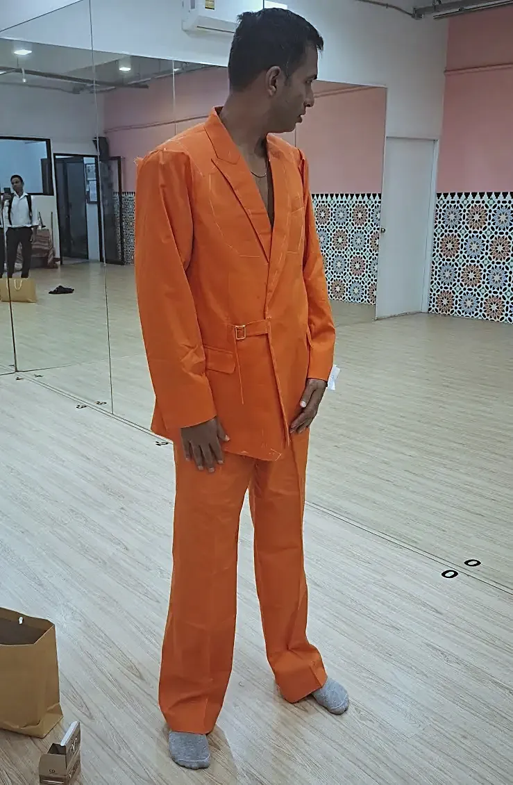 An orange performance suit at the fitting, chalk marks and basting still showing.