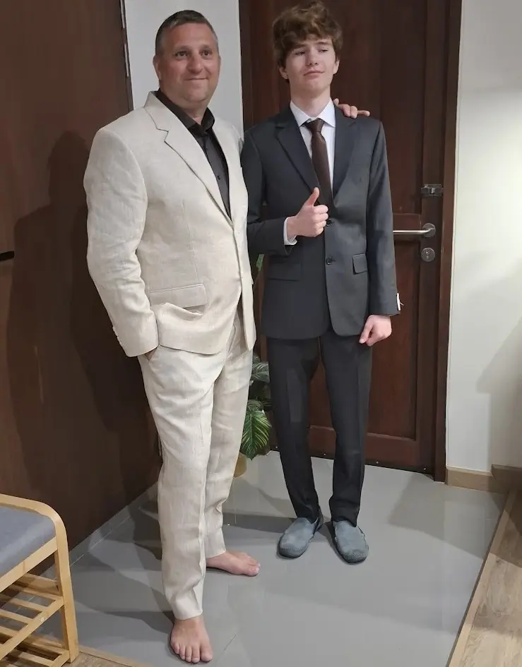 Two customers in finished suits — cream linen and grey worsted — photographed at home after delivery.