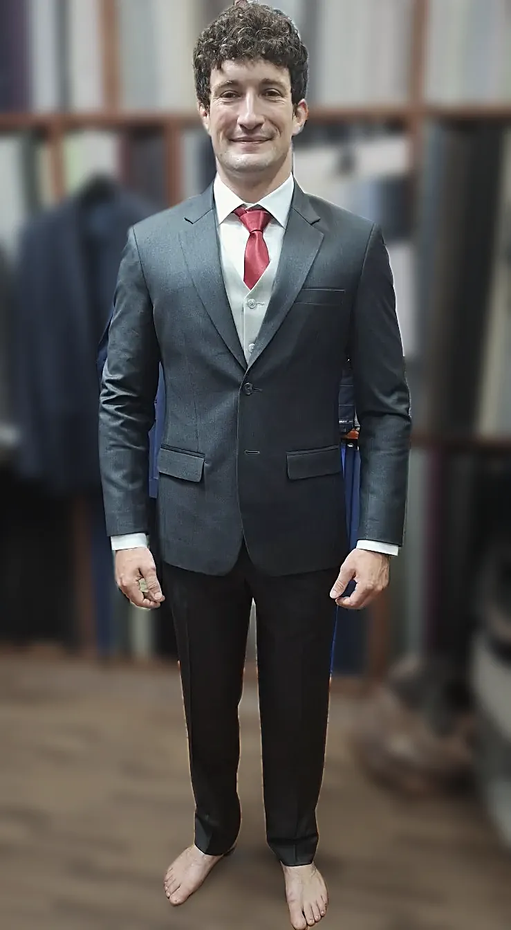 A grey three-piece with a pale waistcoat and a red tie, tried on before the finishing.