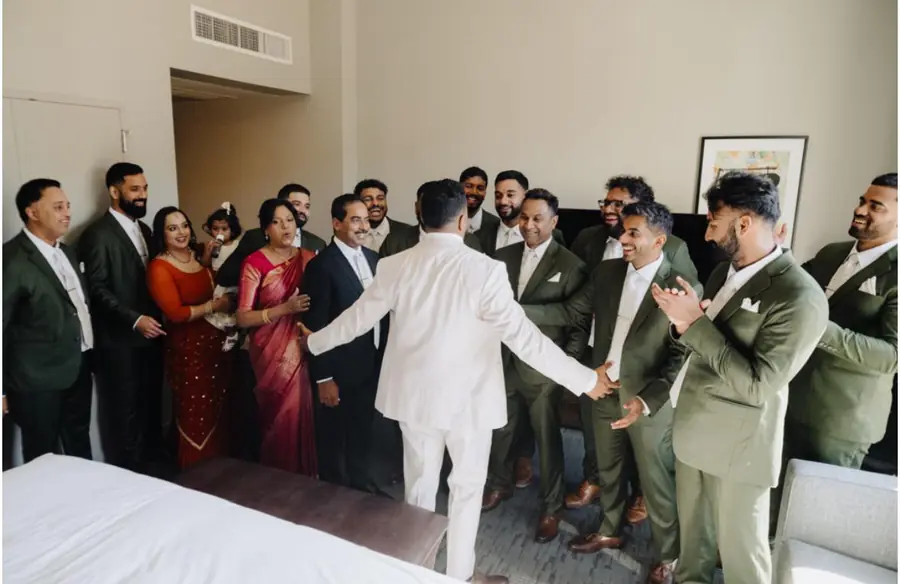 The groom in cream greeting his groomsmen in olive, in the hotel suite before the ceremony.