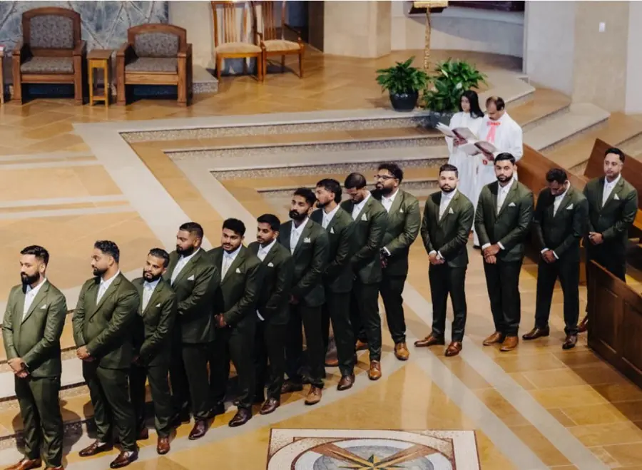 Fourteen groomsmen in olive suits with white pocket squares, lined up during the ceremony.
