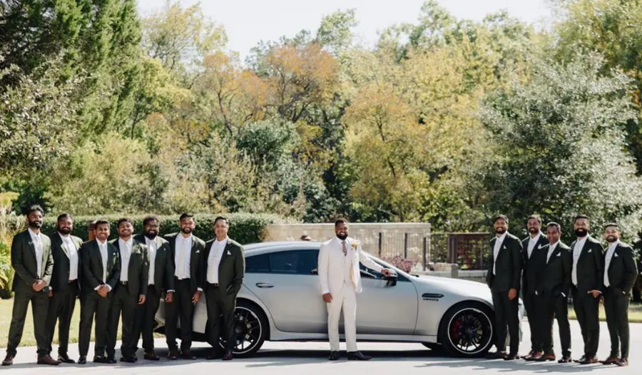 The groom in a cream suit with twelve groomsmen in olive, outside before the ceremony.