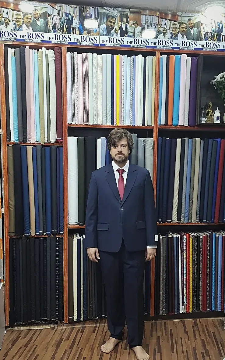 A finished navy suit and red tie, against the wall of suiting it was chosen from.