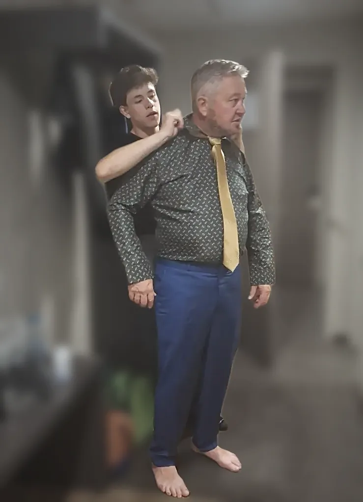 A shirt being checked at the shoulder during a home fitting, the tie loose and the collar still being set.