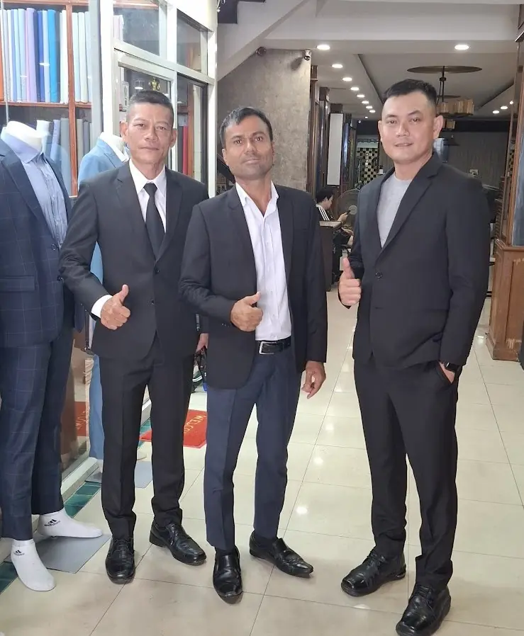 Three finished dark suits with the tailor who measured them.