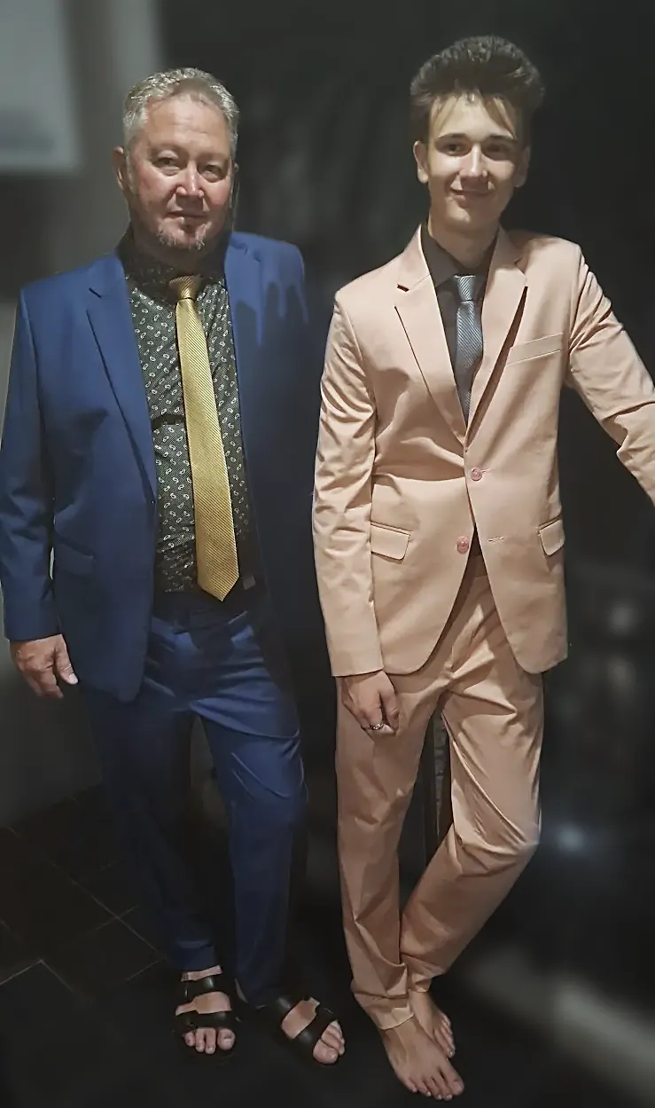 Two finished suits at home: a blue one with a gold tie, and a peach suit cut for a younger wearer.