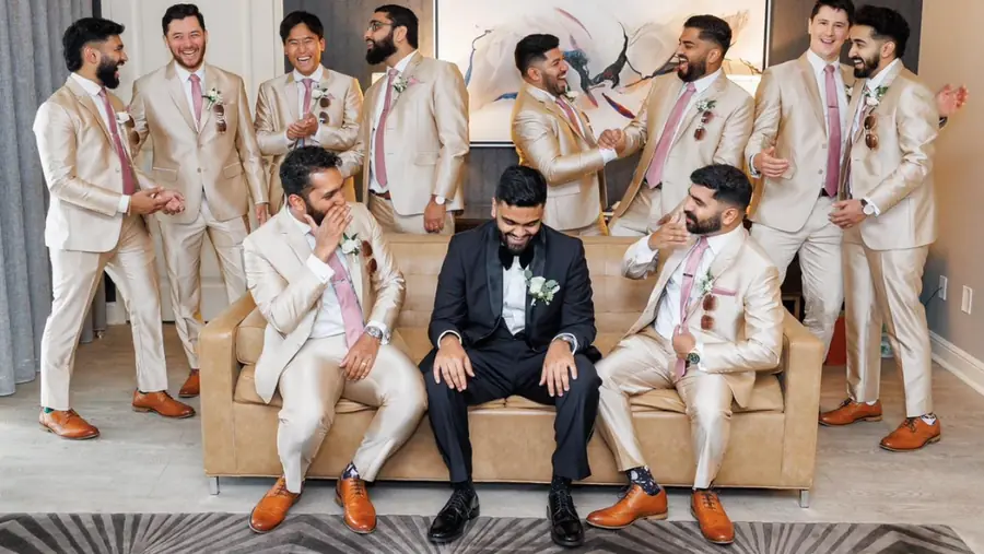 A wedding party in matching cream suits with pink ties, the groom in a black shawl-collar dinner jacket, before the ceremony.
