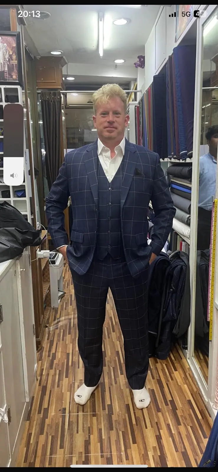 The reviewer in the navy windowpane-check three-piece they ordered, waistcoat buttoned over an open white shirt, photographed in the fitting aisle.