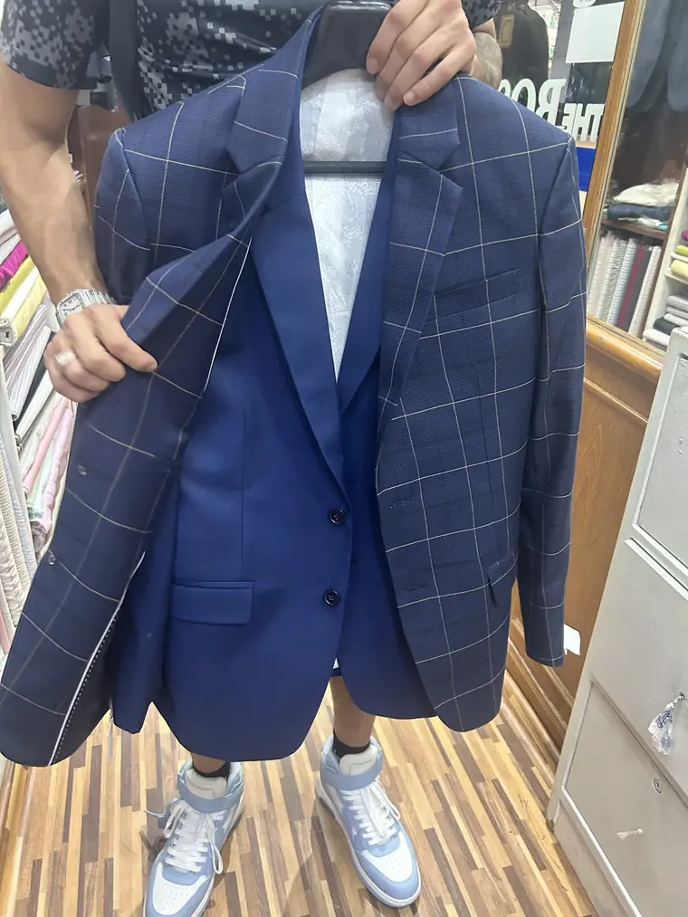 Two finished jackets on one hanger, held open by hand: a navy windowpane check in front of a plain royal blue.