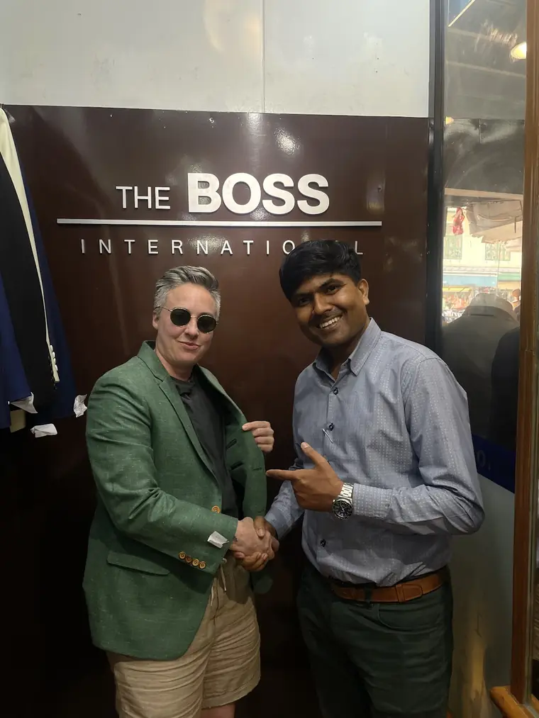 The reviewer in the green blazer they had made, worn over shorts, shaking hands with one of the tailors under The Boss International sign.