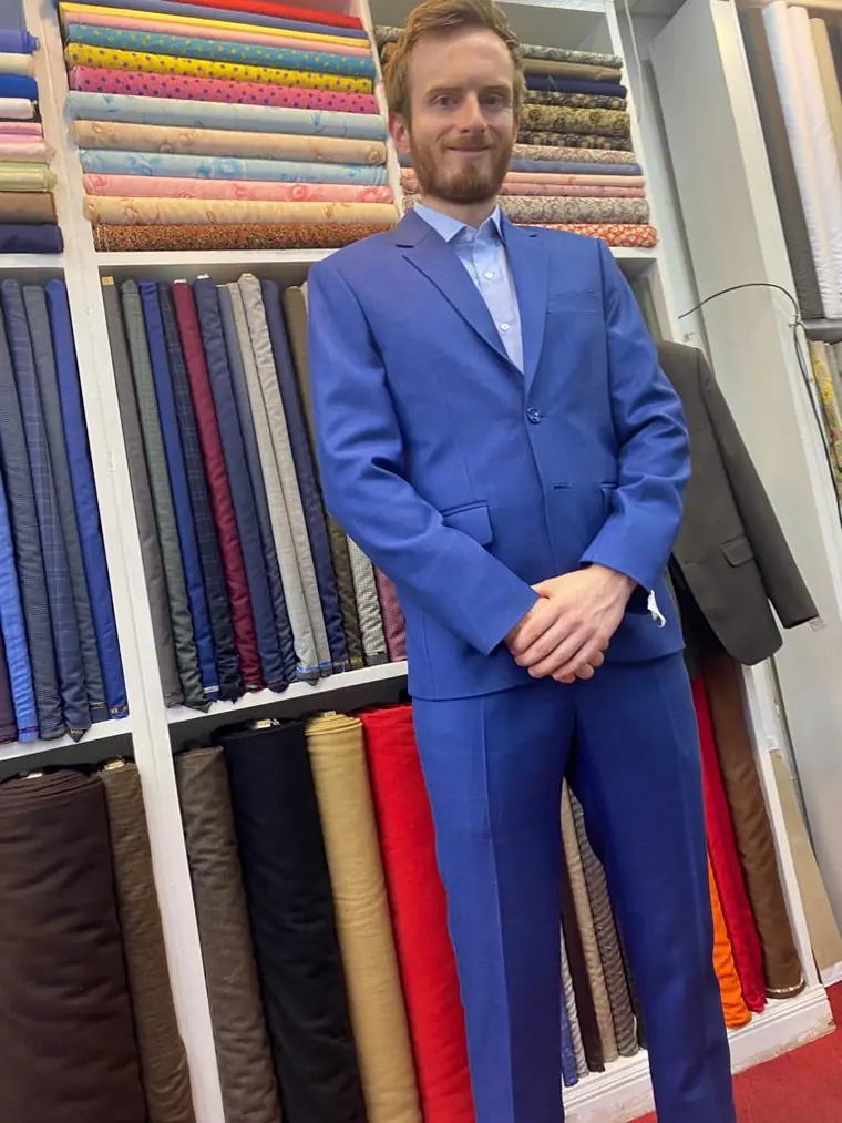 The reviewer in the bright blue two-piece they had made, standing in front of the shelved bolts and rolls of cloth.