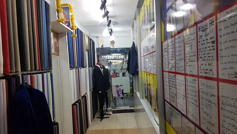 The fitting aisle: shelved bolts of cloth down one side, a suited mannequin at the end, and the wall of handwritten notes customers have left in a dozen languages.