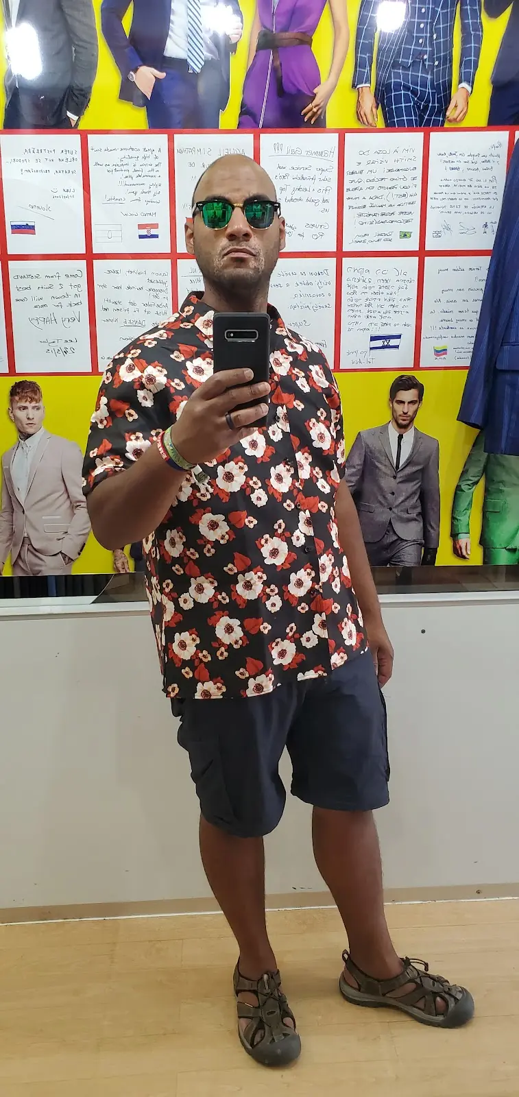 The reviewer’s mirror selfie in the floral short-sleeved shirt they had made, in front of the wall of handwritten notes customers have left in a dozen languages.