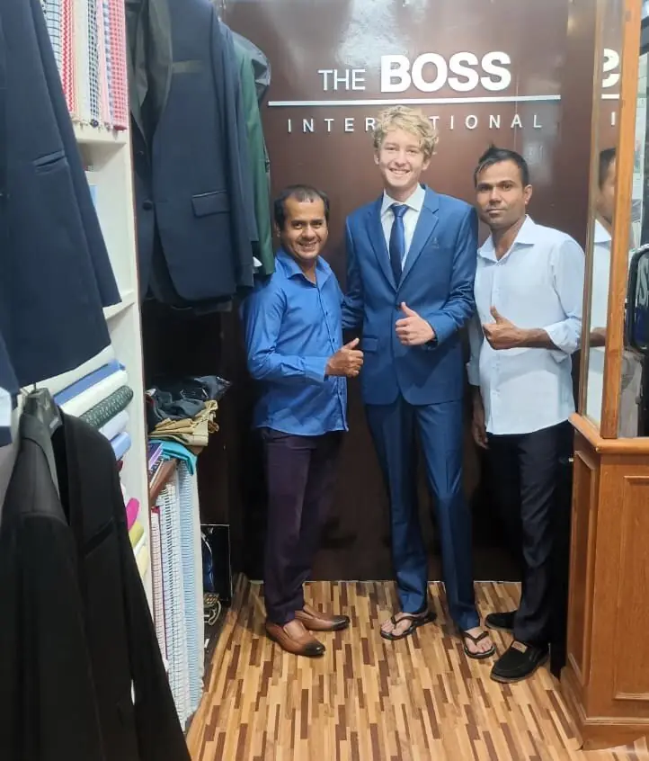 The reviewer in the blue suit and tie they had made, thumbs up between two of the tailors under The Boss International sign.
