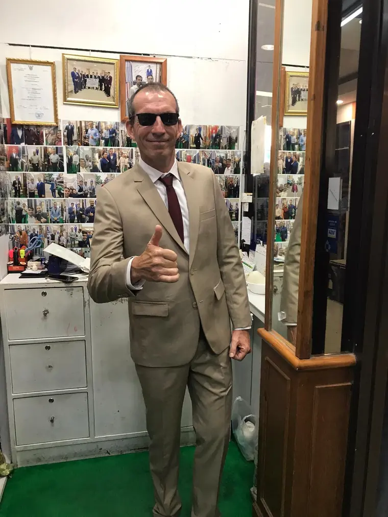 The reviewer in the sand-coloured suit and burgundy tie they had made, thumbs up in front of the board of customer photographs.