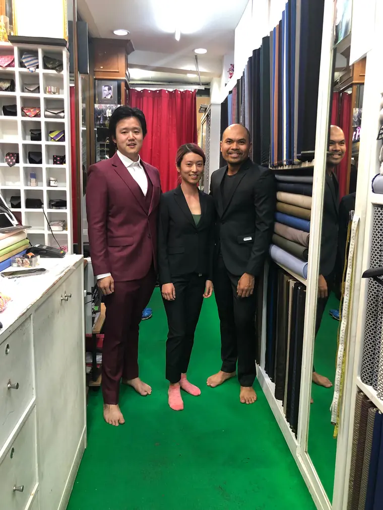 Three finished garments together: a burgundy three-piece, a woman's black trouser suit and a black suit, worn by the customers who ordered them.