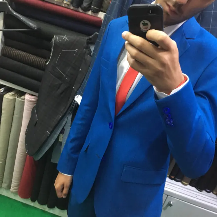 A mirror selfie of a bright blue jacket with contrasting blue buttonholes, worn over a white shirt and red tie, with a chalked and pinned jacket hanging alongside.