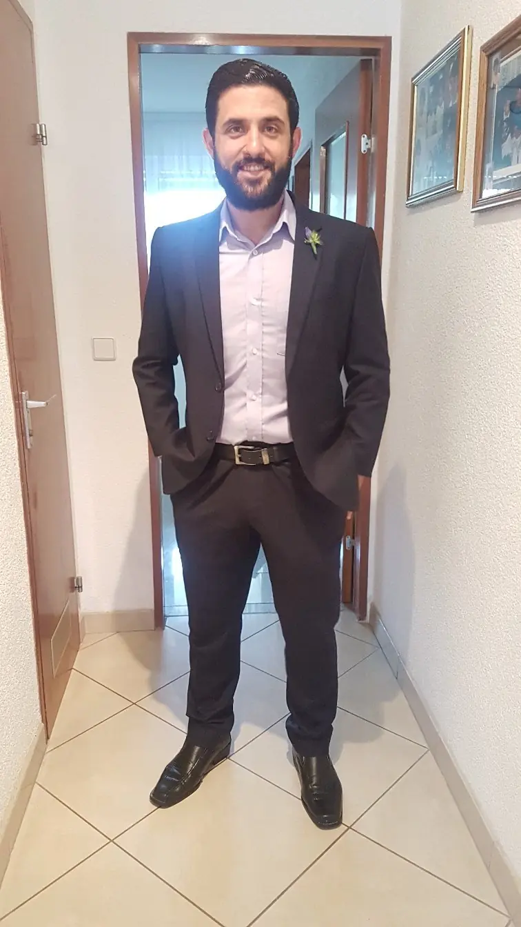 The reviewer wearing the dark suit they had made, photographed at home with a buttonhole flower.