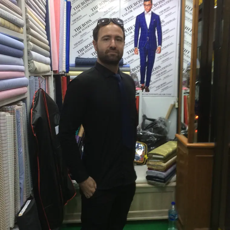 The reviewer carrying a finished garment in its carrier, standing among the shelved bolts of cloth.
