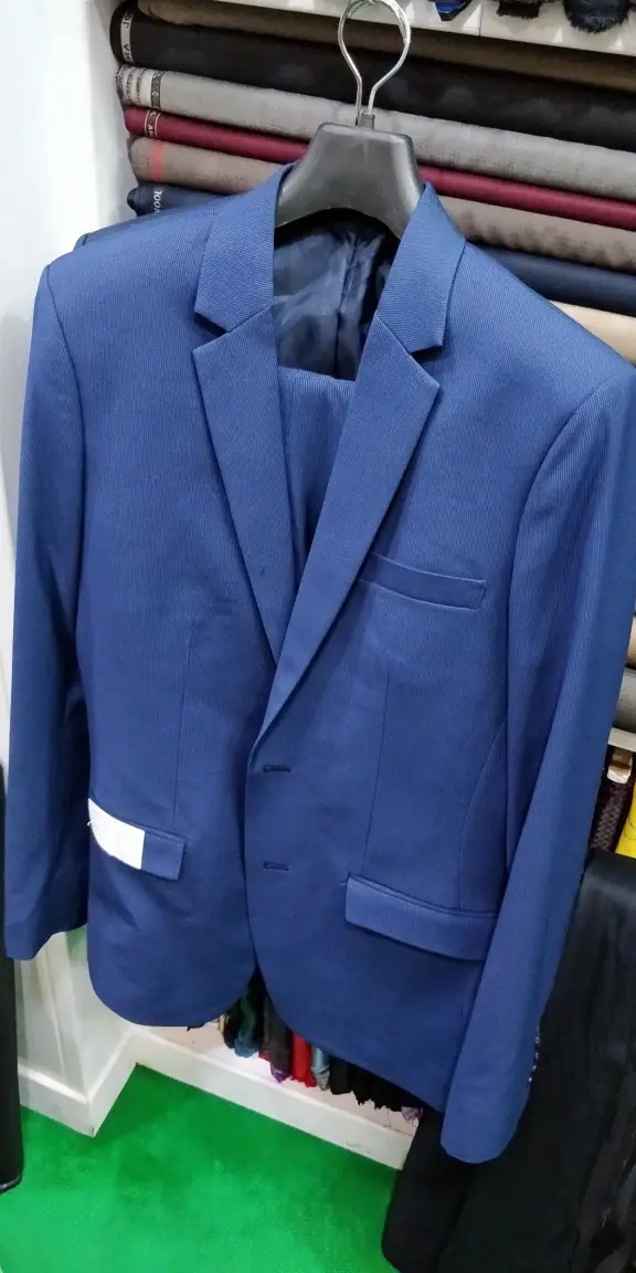 A finished navy jacket on the hanger with the maker's tag still attached, in front of the rolls of cloth.