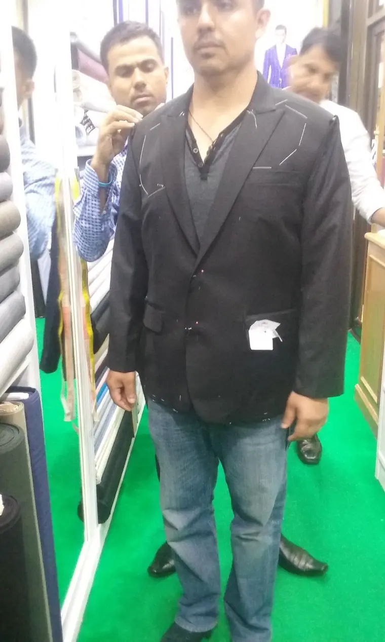 A fitting in progress: the jacket pinned and chalked along the lapel and shoulder while a tailor works on it.
